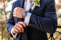 Groom fixing his cufflinks. Handsome groom dressed in dark blue formal suit getting ready for wedding. Elegant groom wedding fashion.