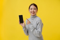 Portrait of female Asian tourist, holding blank template mobile phone for presenting mobile application, grey shirt, isolated on yellow background
