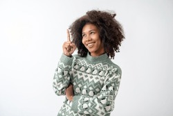 Portrait of young attractive african american woman with curly hair and pointing fore fingers upwards in studio on white background. 