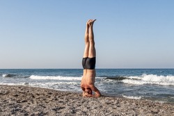 Middle age Man in shorts is doing his morning exercises on the beach by the sea. Headstand