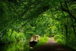 A moored barge rests peacefully on a canal in the beautiful Welsh countryside. lush green verdant trees grow in abundance in the pleasant natural surroundings of the Brecon and Monmouth canal