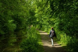 A female hiker on a footpath next to a canal in the Welsh countryside. lush green verdant trees grow in abundance in the pleasant natural surroundings of the Brecon and Monmouth canal