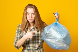 Teen girl holding plastic trash bag on yellow background. Waste sorting and sustainability concept.