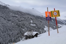 winter landscape with only color coming from signs warning for avalanges (signs read 'closed' and 'danger of avalanche')