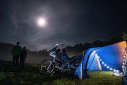 Camping, blue tent with light, touring motorcycle for travel. The concept of recreation and tourism. Space for text, selective focus. Mist, fog and moonlight. Couple man and woman.