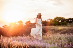 The beautiful girl in the dress is having fun on the hill at sunset. The girl is walking down the hill at sunset