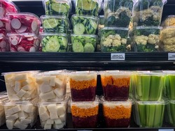 Freshly cut veggies in plastic containers arranged on shelves at grocery store 