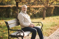 Old gray-haired man rest on the bench in autumn park