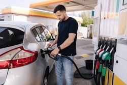 Handsome young man refueling car at gas station. Male filling diesel at gasoline fuel in car using a fuel nozzle. Petrol concept. Side view