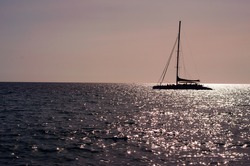 The sailboat (yacht) goes forward against the background of the horizon and the pink sunset