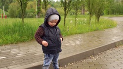Portrait of a little boy in a waistcoat in a rainy day in a park, hands in his pockets.