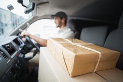 Delivery driver driving van with parcels on seat outside the warehouse
