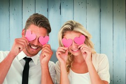 Attractive young couple holding pink hearts over eyes against wooden planks