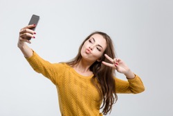 Portrait of a young attractive woman making selfie photo on smartphone isolated on a white background