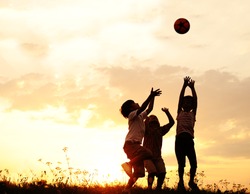 Group of happy children playing with ball on meadow, sunset, summertime