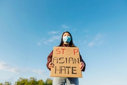 Young chinese woman protesting against hate in the outbreak situation of coronavirus infection or Covid-19 - Stop asian hate fight campaign - Focus on banner