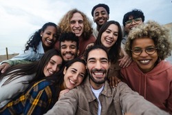 Big group portrait of diverse young people together outdoors - Multiracial happy millennial male and female friends having fun together - Unity and friendship concept - Focus on man in the center