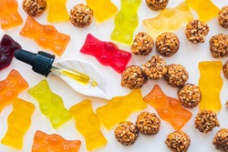 Gummy bears, cbd cookies and thd oil dropper in white backdrop. THD or cannabis sweets in form of gelatine gummi bears and essential oil pipette background: calming edible food supplements