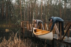 Canoeing lifestyle, autumn or spring season. Two men put a canadian canoe boat on water at the forest lake