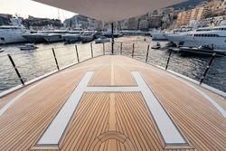The front deck of huge yacht in port of Monaco at sunset, the place for landing of helicopter, a lot of motorboats are on background, the chrome plated handrail, megayacht is moored in marina, dusk