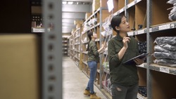 female warehouse worker checking stock of cables in stockroom. two asian chinese women coworkers standing and counting parcels in storehouse. young lady colleagues in uniform stock taking in depot.