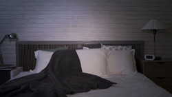 interior of empty bedroom at night, with unmade bed and tv left on at modern living space with white bedding and grey blanket 