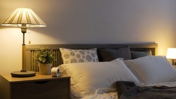 cozy modern illuminated bedroom with a bedside lamp and white double bed covered by grey sheet cover in an apartment.