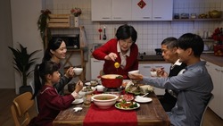 senior mistress of the family grandmother standing up and offering food to each member with chopsticks at dinner table during Chinese new year's eve reunion meal at home
