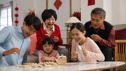 family members laughing at young mother as she makes toy wood blocks fall. big family enjoying tumbling tower game during spring festival. translation of chinese text: spring
