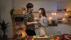 asian romantic couple flirting with each other with wine on valentine’s night date at home in the kitchen. the man gently touching girlfriend’s shoulder while talking with hand gestures