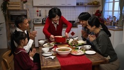 happy grandmother serving delicious food on dining table as her family members clapping hands for her. getting ready for big meal on chinese new year's eve