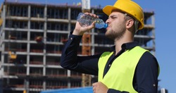 Engineer Man Drink Water in a Hot Summer Day,  Worker Male Have a Break near Under Construction Building