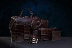 Brown crocodile leather men's accesories - handbag, purse; clutch, two wallets and belt on dark blue background. Fashion and shopping concept