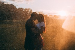 Lovers in the rain. The guy hugs the girl. Raindrops against the sunset background.