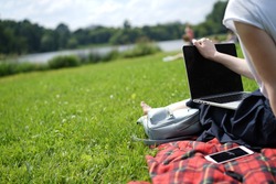 Young woman's legs on the green grass with open laptop. Girl's hands on keyboard. Distance learning concept