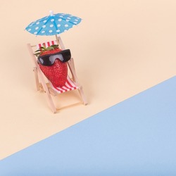 Creative fun idea made of deck chair, sun umbrella and strawberry with sunglasses on a beach. Minimal  summer vacation concept.
