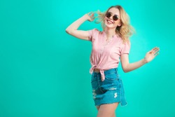 Portrait of cheerful pretty caucasian girl with long blond curly hair, wearing sunglasses gesturing with arms looking at camera full of happiness isolated on blue background