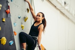 Young sporty caucasian woman practicing rock climbing on artificial wall indoors. Active lifestyle and bouldering concept.