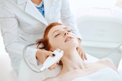 Woman receiving electric facial ultrusound peeling at modern beauty salon. Female patient getting radio frequency lifting on her face.