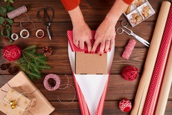Woman s hands wrapping Christmas gift, close up. Unprepared christmas presents on wooden background with decor elements and items, top view. Christmas or New year DIY packing Concept.