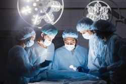 Shot of a multiracial surgeon team consists of trained surgeons, trauma specialists and plastic surgeons, consulting during difficult operation proceed, standing before unconscious patient in O.R.