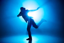 A dark silhouette of a singer on the stage, dancing alone during performance on dark blue neon background with smoke and lights.