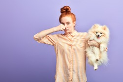 funny girl with stylish striped shirt closing her nose, as the dog is farting. close up portrait. unpredictable situation, isolated blue background, studio shot.