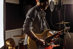 young caucasian gorgeous musician play electric guitar and sing on microphone in recording studio. rockstar perform music. man preparing, practicing before concert.