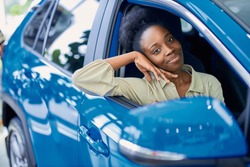 happy young black woman in dealership, beautiful lady came to buy automobile,she liked one of cars represented in dealership