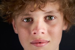 close-up portrait of calm caucasian boy looking at camera, male teenager isolated over black background