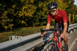 Young caucasian cyclist in black helmet, protective glasses and active wear dynamically riding bicycle. Man preparing for competitions and races on fresh air. outdoors in nature, on road