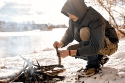 young man on expedition, making fire in forest, wild nature. bonfire by male person. fire made of wood. bushcraft, adventure, travel, tourism and camping concept. extreme condition