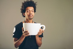 young happy african man holding a funny huge and oversized cup of black coffee in caffeine addiction concept
