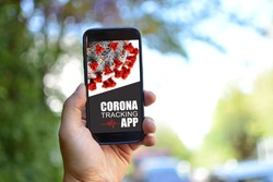 Tracking App concept for Corona virus with hand holding mobile phone with application design on screen in front of blurry outdoor background